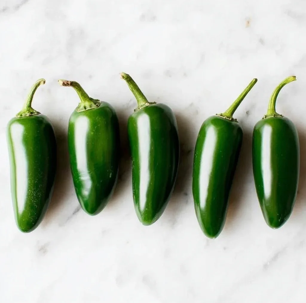 Whole fresh jalapeno peppers lined up on a marble surface before making pickled jalapenos