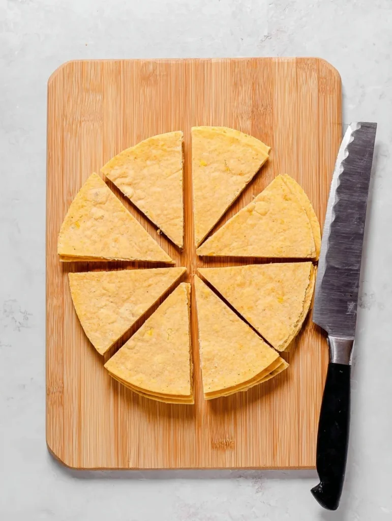Corn tortillas cut into triangles on a wooden cutting board with a knife, ready to make tortilla chips in the air fryer