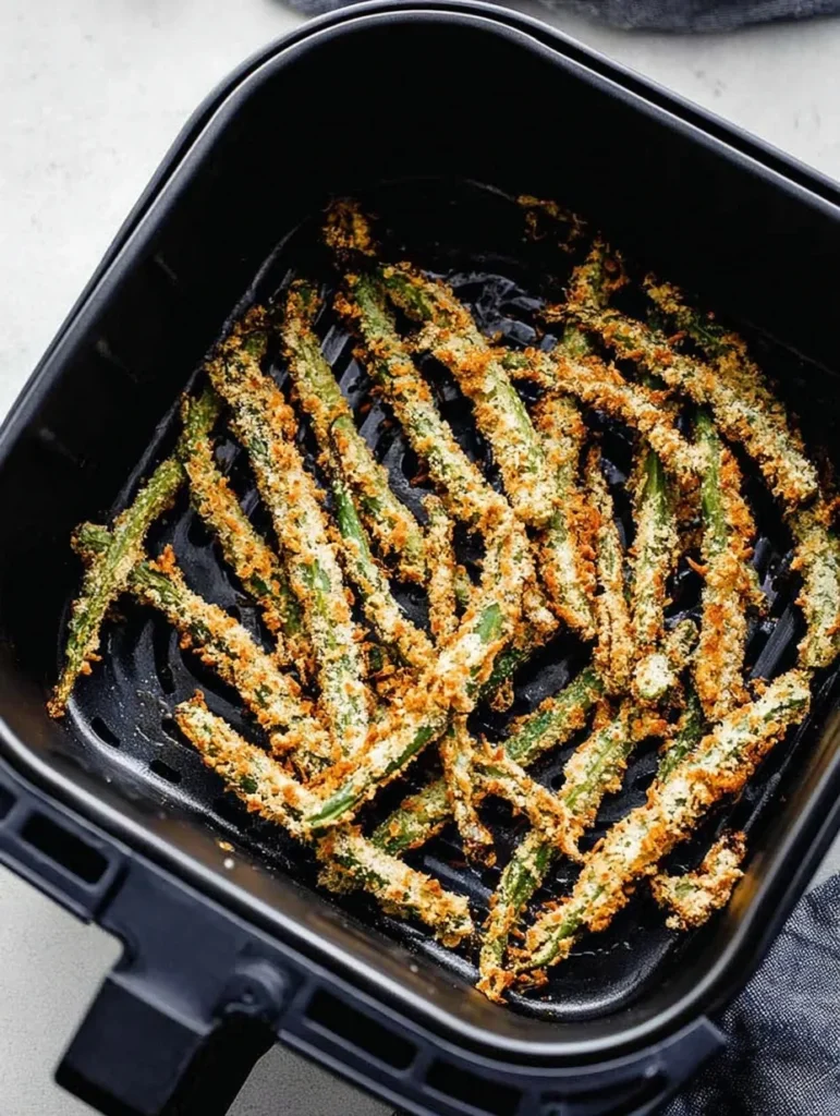 Golden brown air fryer green bean fries inside the basket after cooking.
