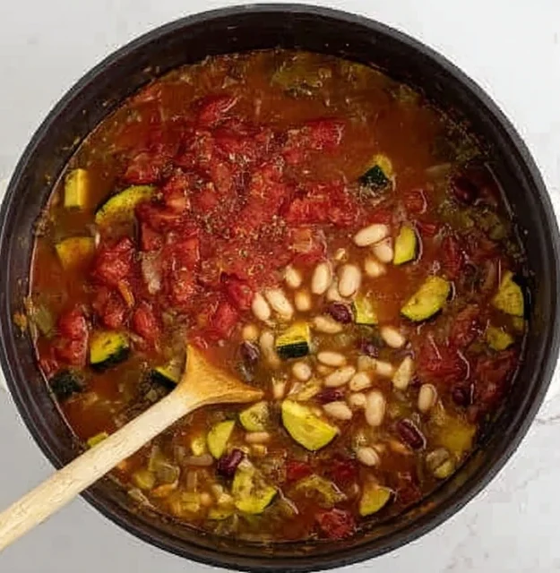 Beans simmering in a pot of vegetable broth with tomatoes and vegetables while making minestrone soup