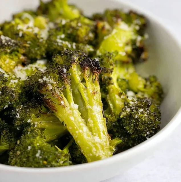 Crispy parmesan-roasted broccoli florets served in a white bowl, golden on the edges and oven roasted to perfection