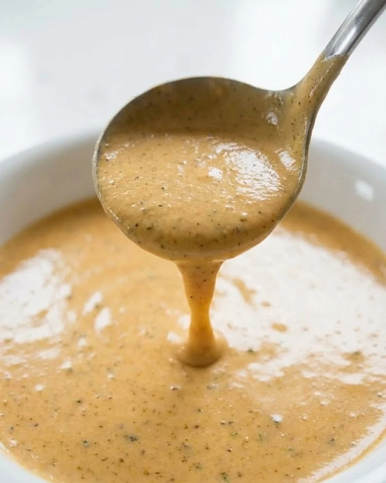 Creamy Cajun Alfredo sauce dripping from a spoon with smooth glossy texture and visible Cajun seasoning