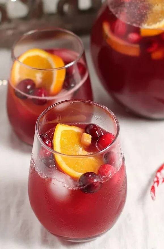 Non-alcoholic holiday punch with cranberry juice, orange slices, and fresh cranberries served in glasses and a pitcher