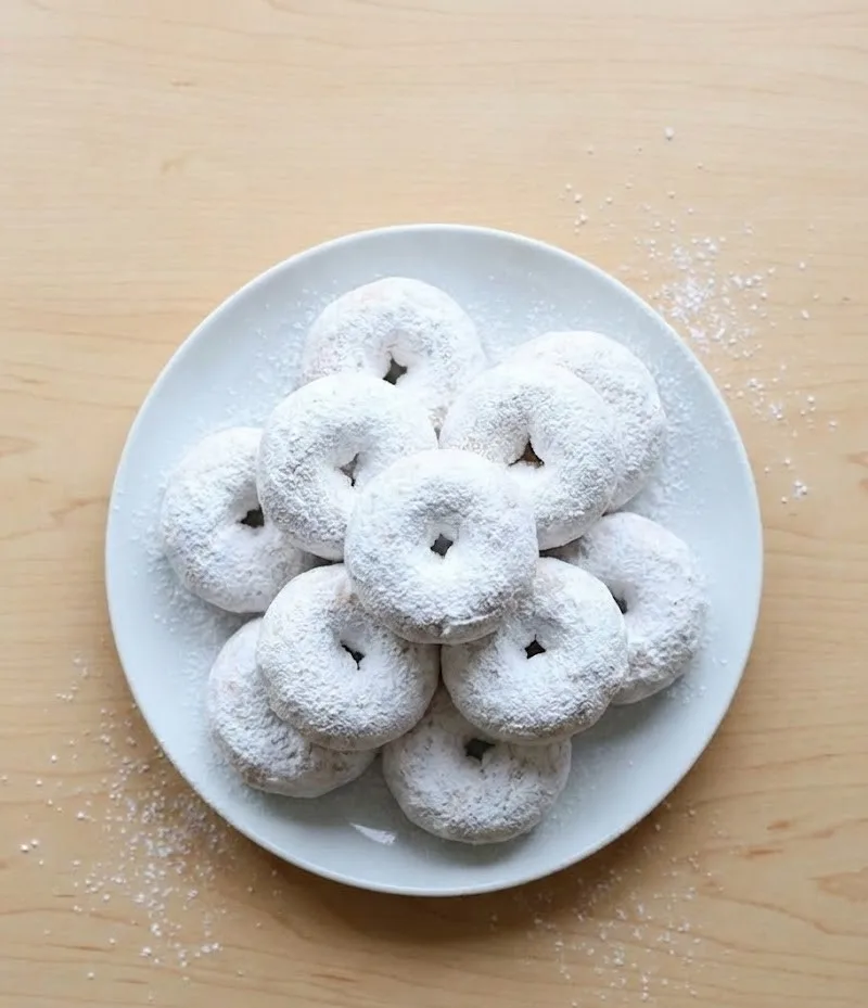 Snowball donuts coated in powdered sugar arranged on a white plate top view
