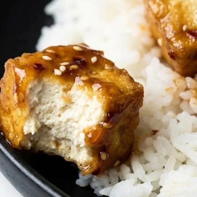 Close up of vegan honey garlic tofu with sticky glaze and sesame seeds served on white rice
