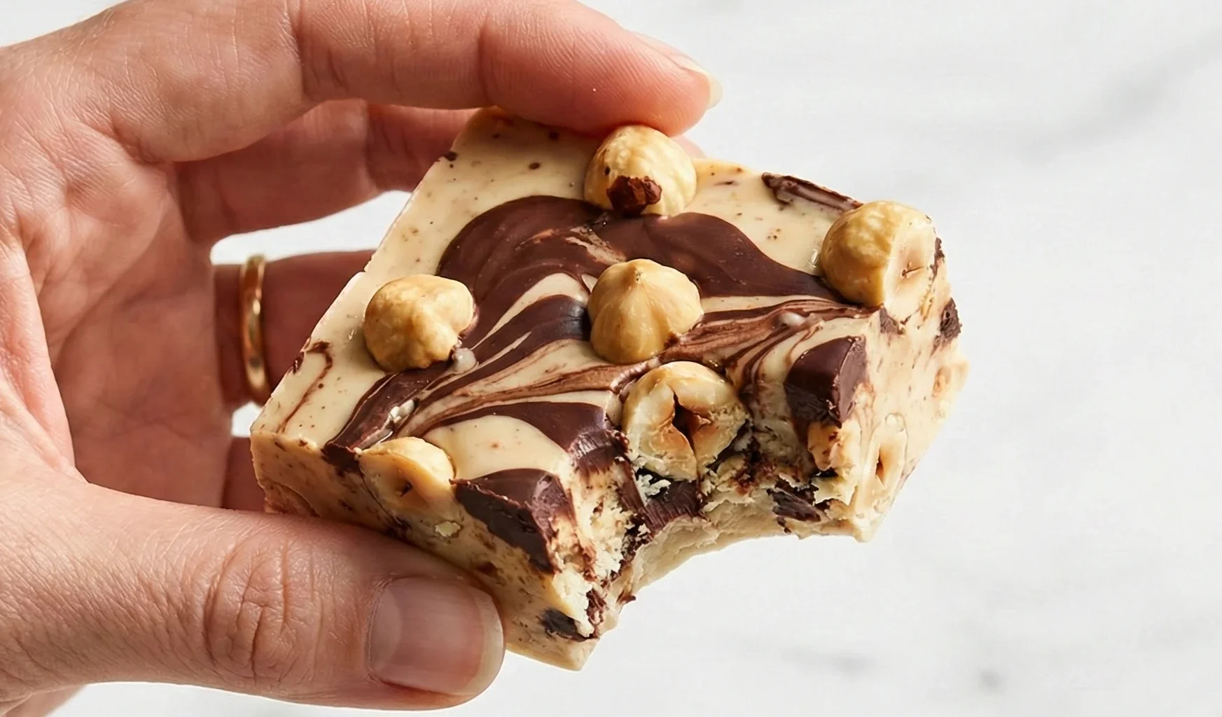 Hand holding bitten Hazelnut Chocolate Nougat square showing chewy texture and whole hazelnuts